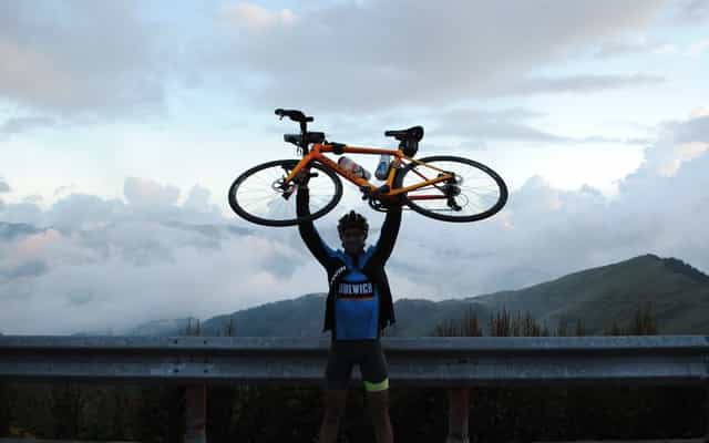 Cyclist holding bike overhead in celebration at Wuling Pass summit above the clouds