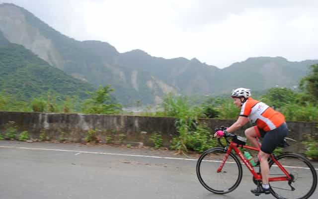 Cyclist riding near Lishan with mountain cliffs in the background, Taiwan
