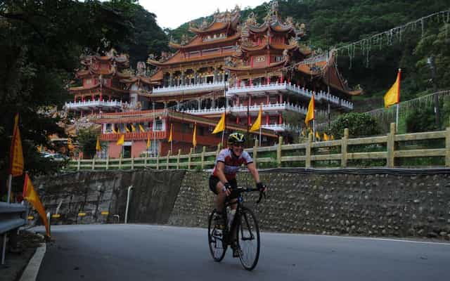 Cyclist riding past an ornate hillside temple near Jiufen, Taiwan
