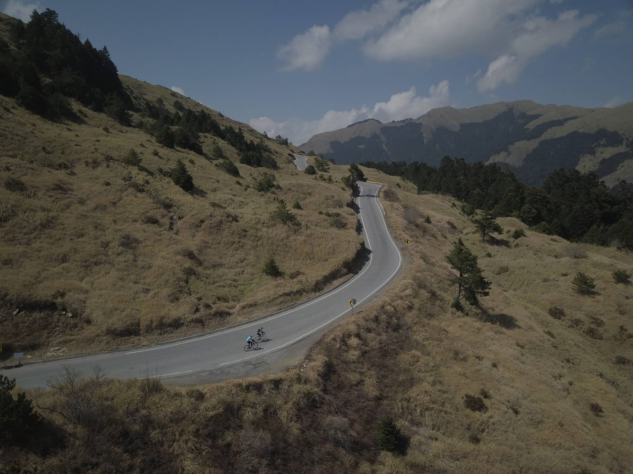 Cyclists riding the upper alpine section of the Taiwan KOM route through grassland with forested peaks behind