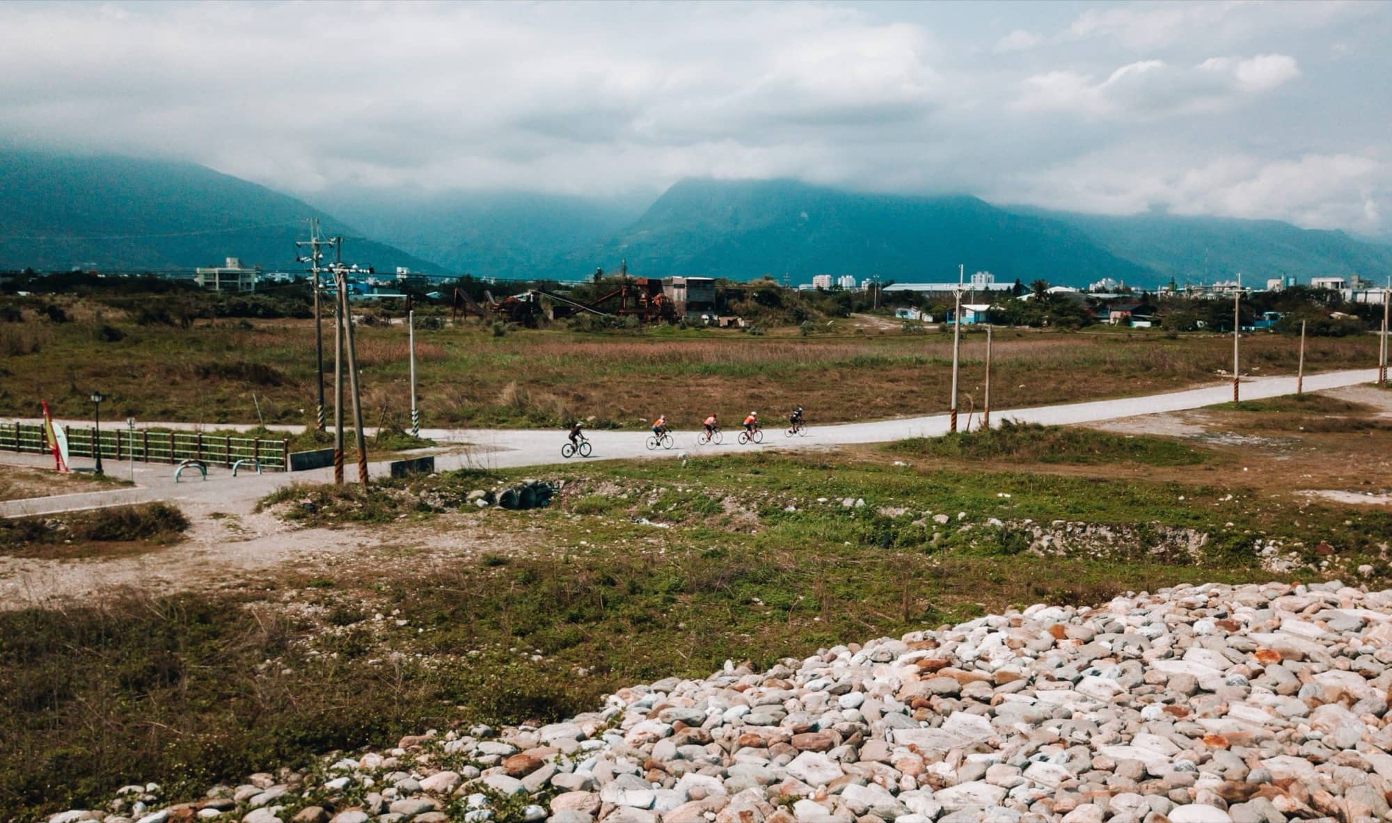 Three cyclists on a quiet path through Taiwan's Rift Valley with layered mountains and low cloud behind