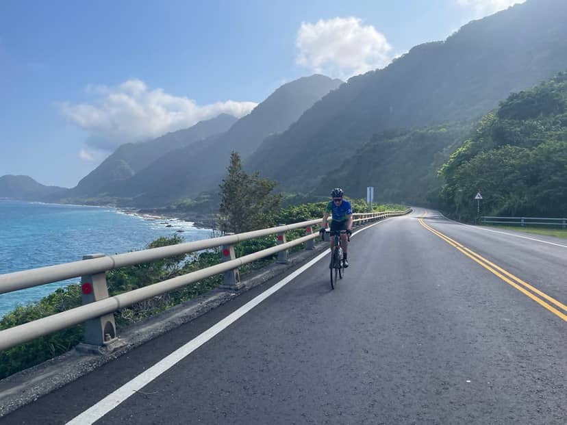 Cyclist riding Taiwan's east coast highway with dramatic mountains dropping into the Pacific Ocean