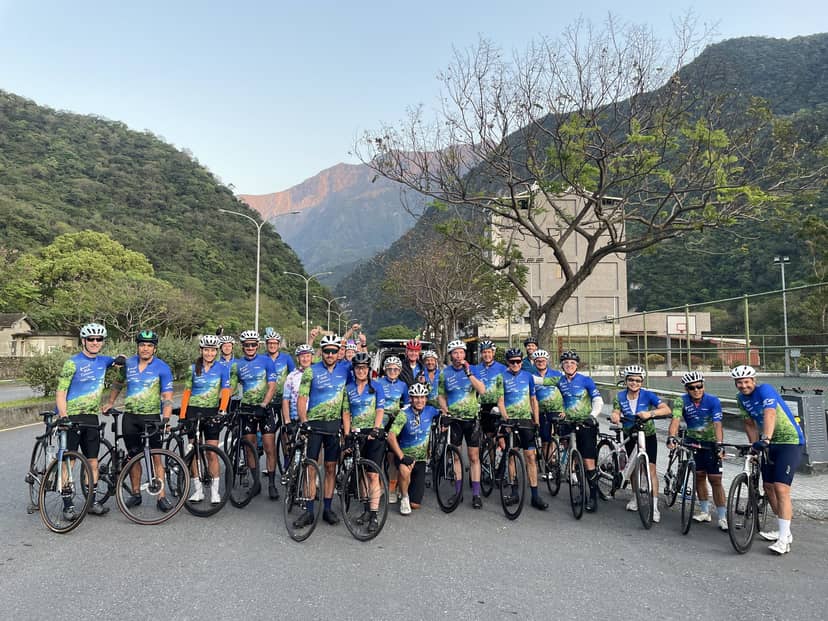 Large cycling group in matching blue club jerseys lined up with bikes on a quiet Taiwanese mountain road at sunrise