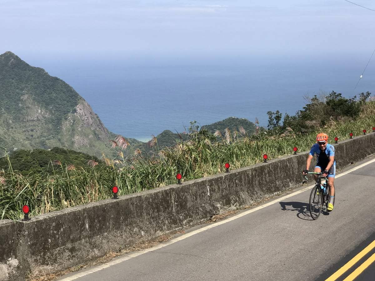 Cyclist riding their own road bike along a dramatic Taiwan coastal mountain road with the Pacific Ocean below