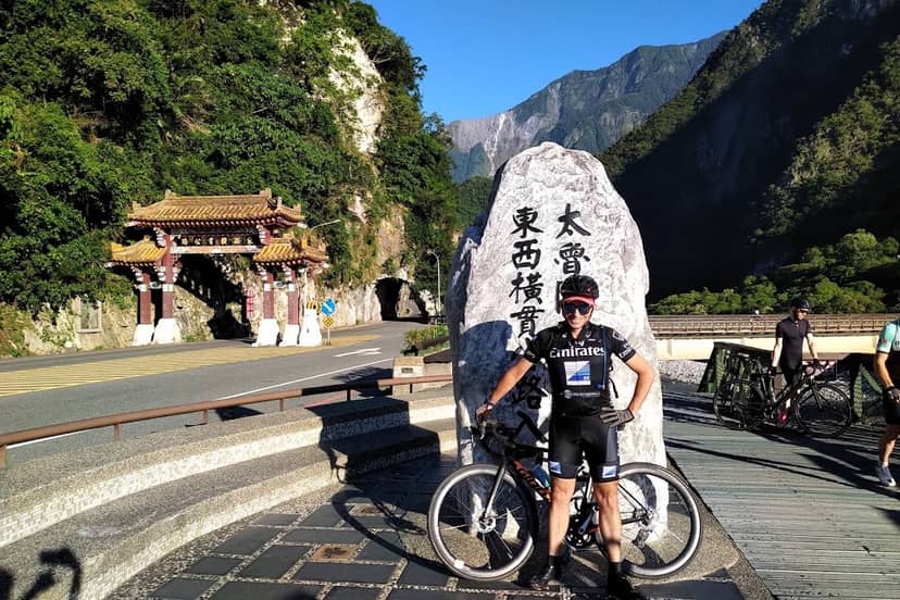 Cyclist posing at the entrance gate to Taroko Gorge National Park with marble cliffs and blue sky behind