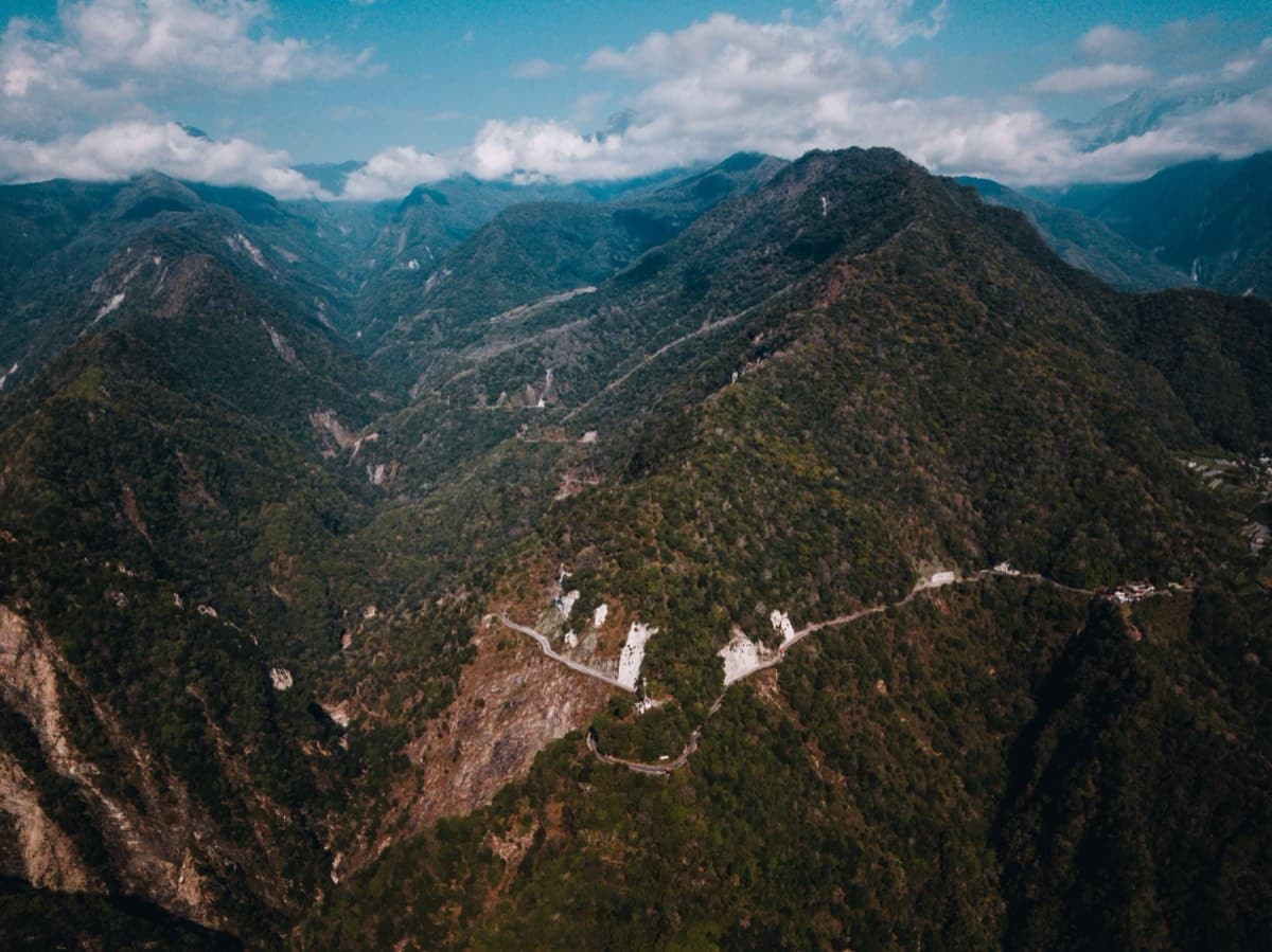 Aerial drone view of dramatic mountain ridges in Taiwan's central range, a switchback road visible winding through the forested valleys below
