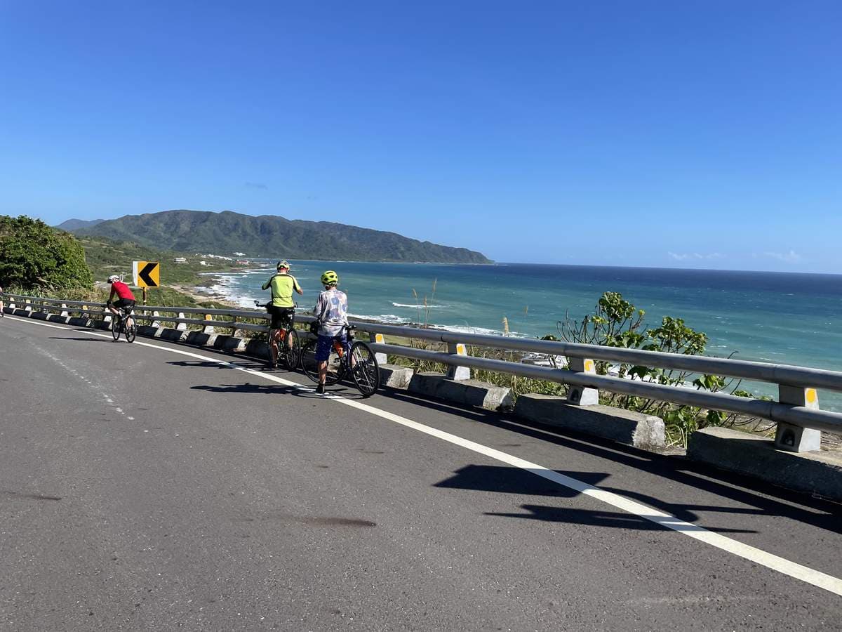 Cyclists pulled up at the roadside looking out over turquoise Pacific water and coastal mountains on the Taiwan east coast