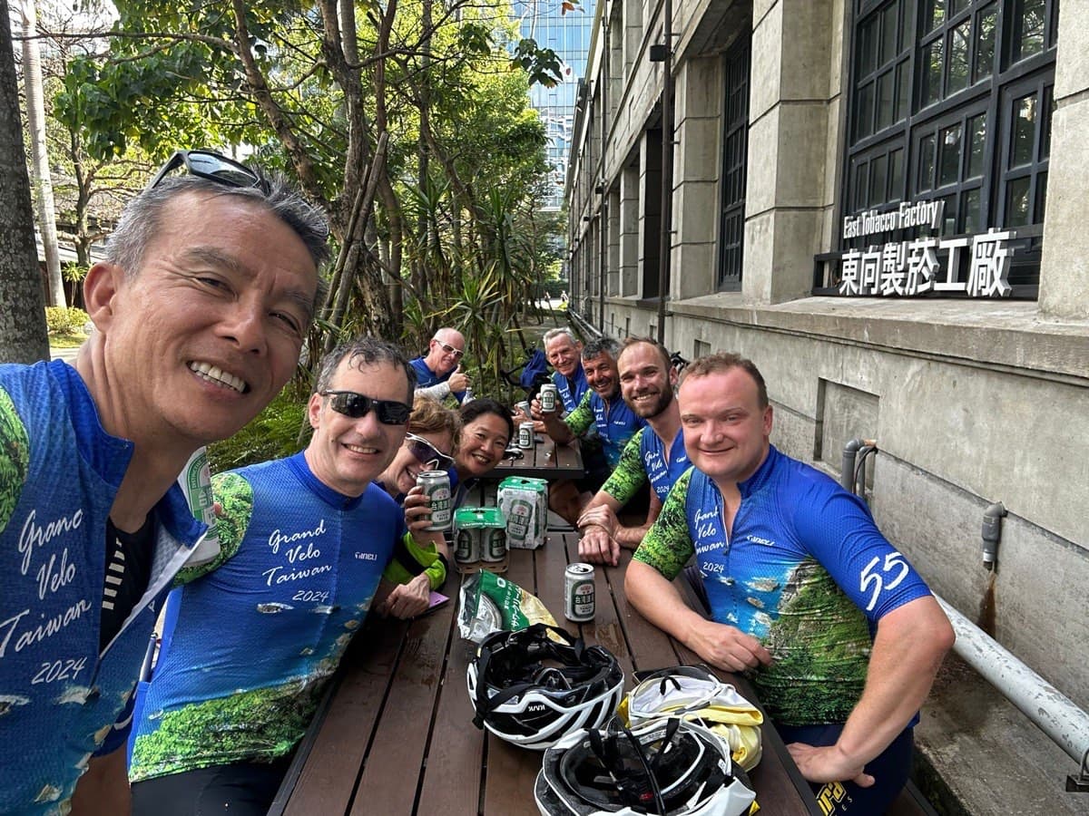 Pedal Taiwan group relaxing at an outdoor restaurant table after a ride, helmets on the table, matching jerseys, cold drinks