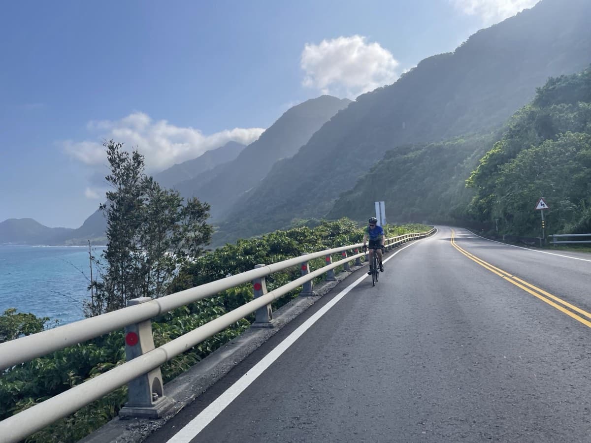 Cyclist on Taiwan's east coast highway with turquoise Pacific Ocean on the left and dramatic green mountains rising ahead