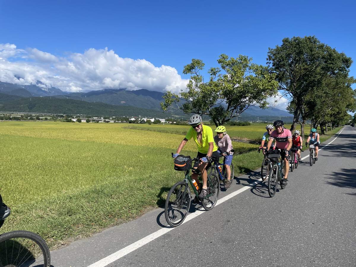 Group of riders on a flat road through the East Rift Valley with rice paddies on one side and the central mountain range in the distance