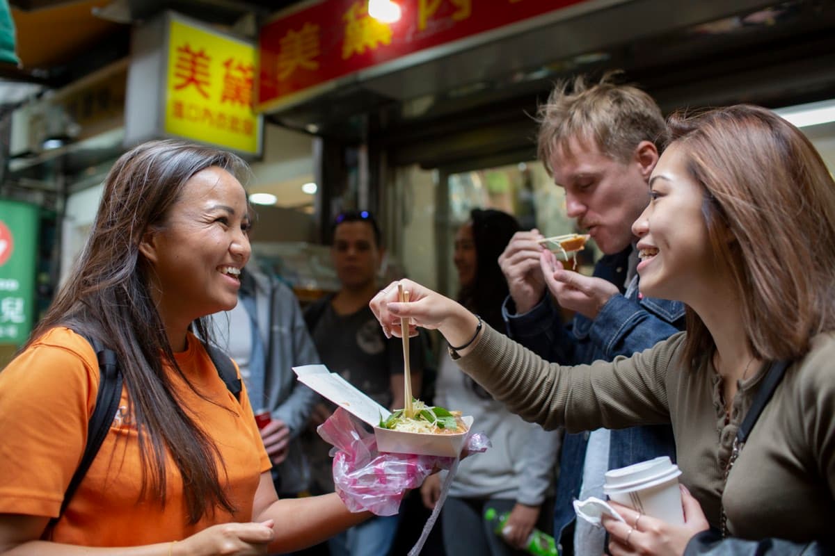 Local Taiwanese guide sharing street food with visiting cyclists outside a night market stall