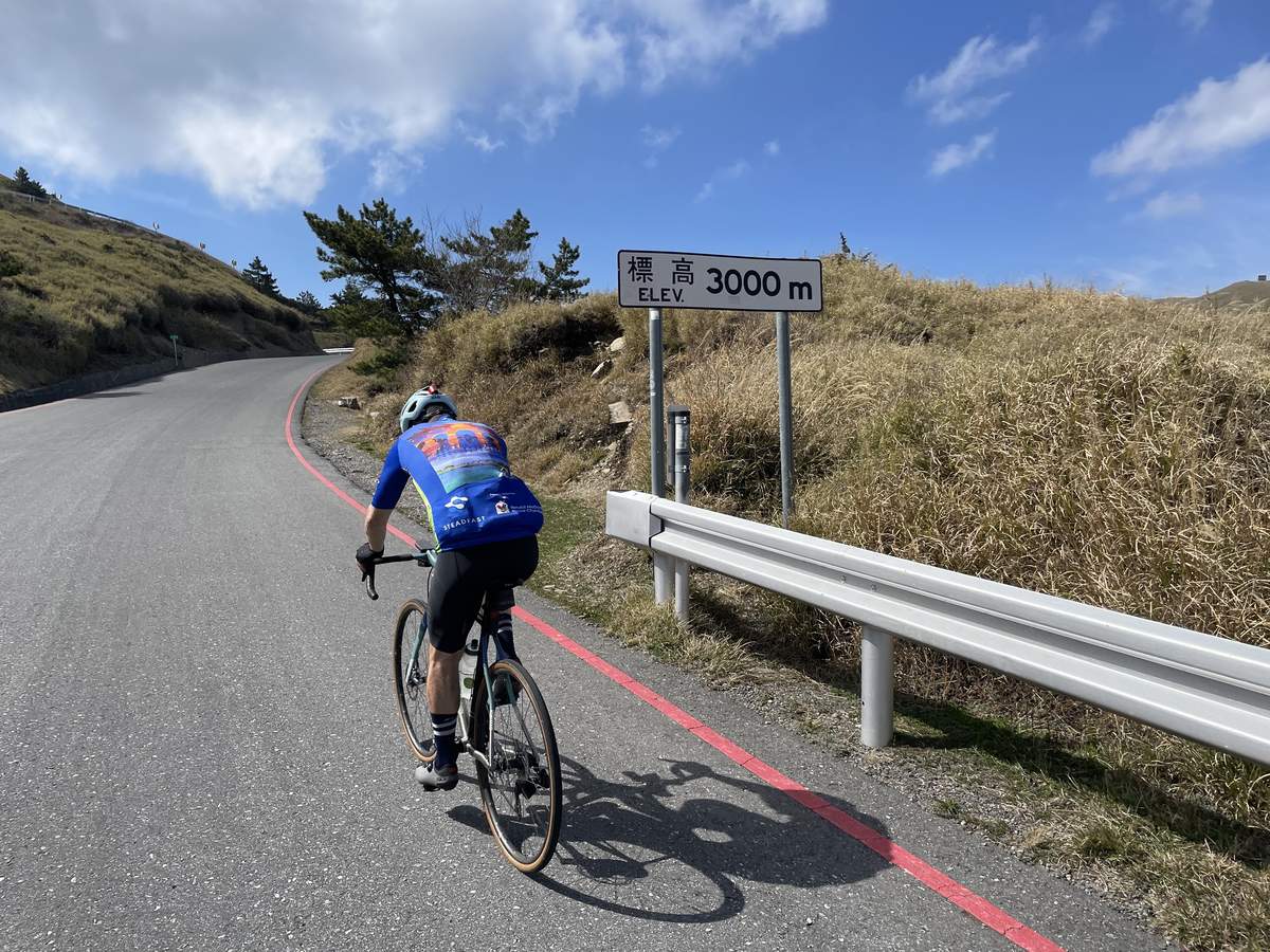 Cyclist in blue jersey climbing past the 3000m elevation sign near the summit of the Taiwan KOM route