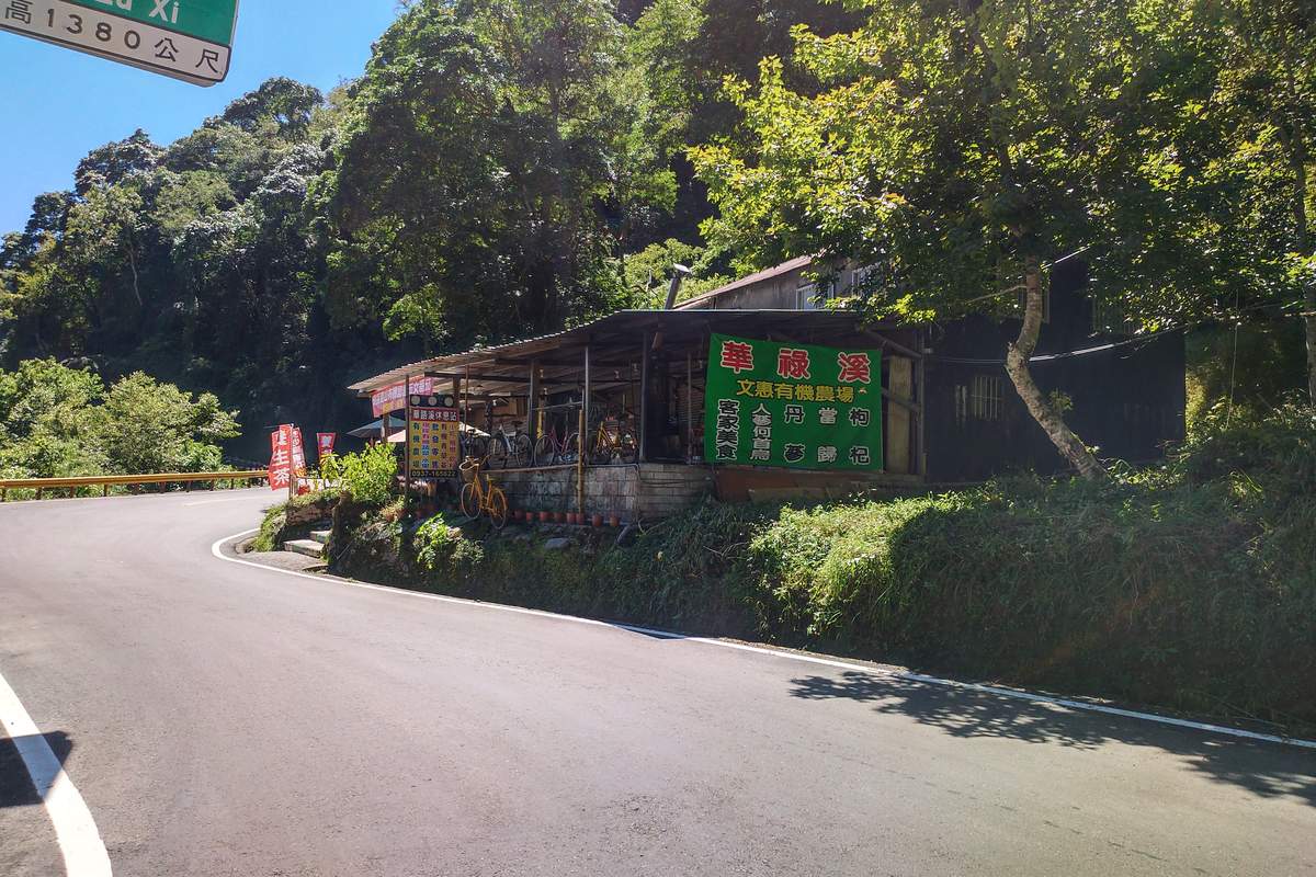 A roadside cycling food stall on a Taiwan mountain road at the 1380m elevation marker, with green Chinese signage and lush forest behind